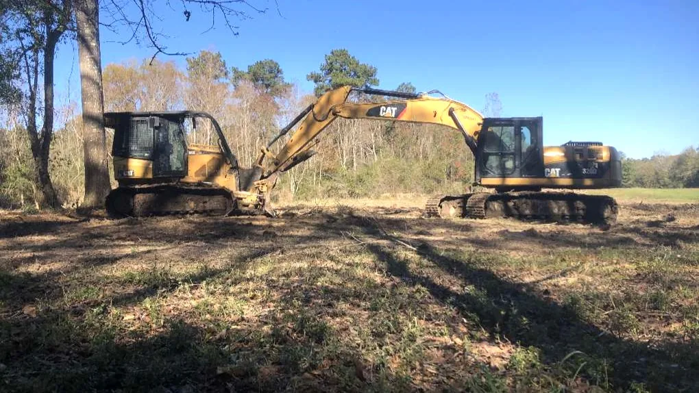 Crawler dozer and excavator on freshly cleared ground at the edge of the woods, land clearing