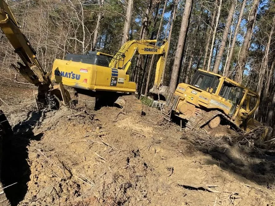 Excavator and crawler dozer clearing roots and clay in a pine stand, land clearing