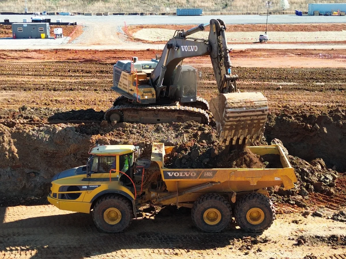 Excavator loading an articulated hauler on a large industrial site, civil construction