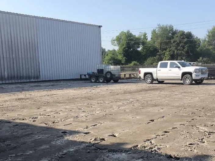 Graded gravel yard beside a metal plant building with a pickup and a utility trailer, civil construction