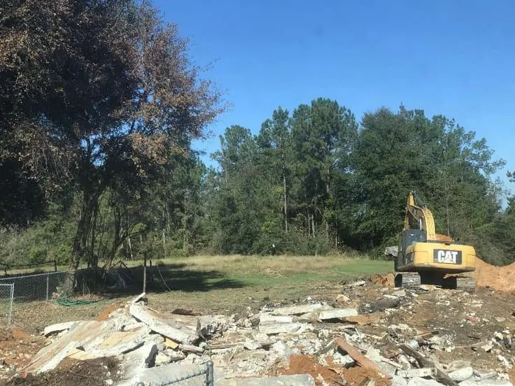 Excavator on a lot after a house was torn down, with broken slab and brick rubble in front, demolition
