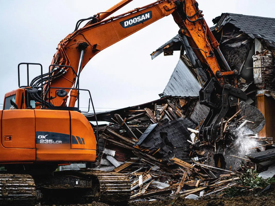 Excavator with a demolition grapple tearing down a two story house, demolition