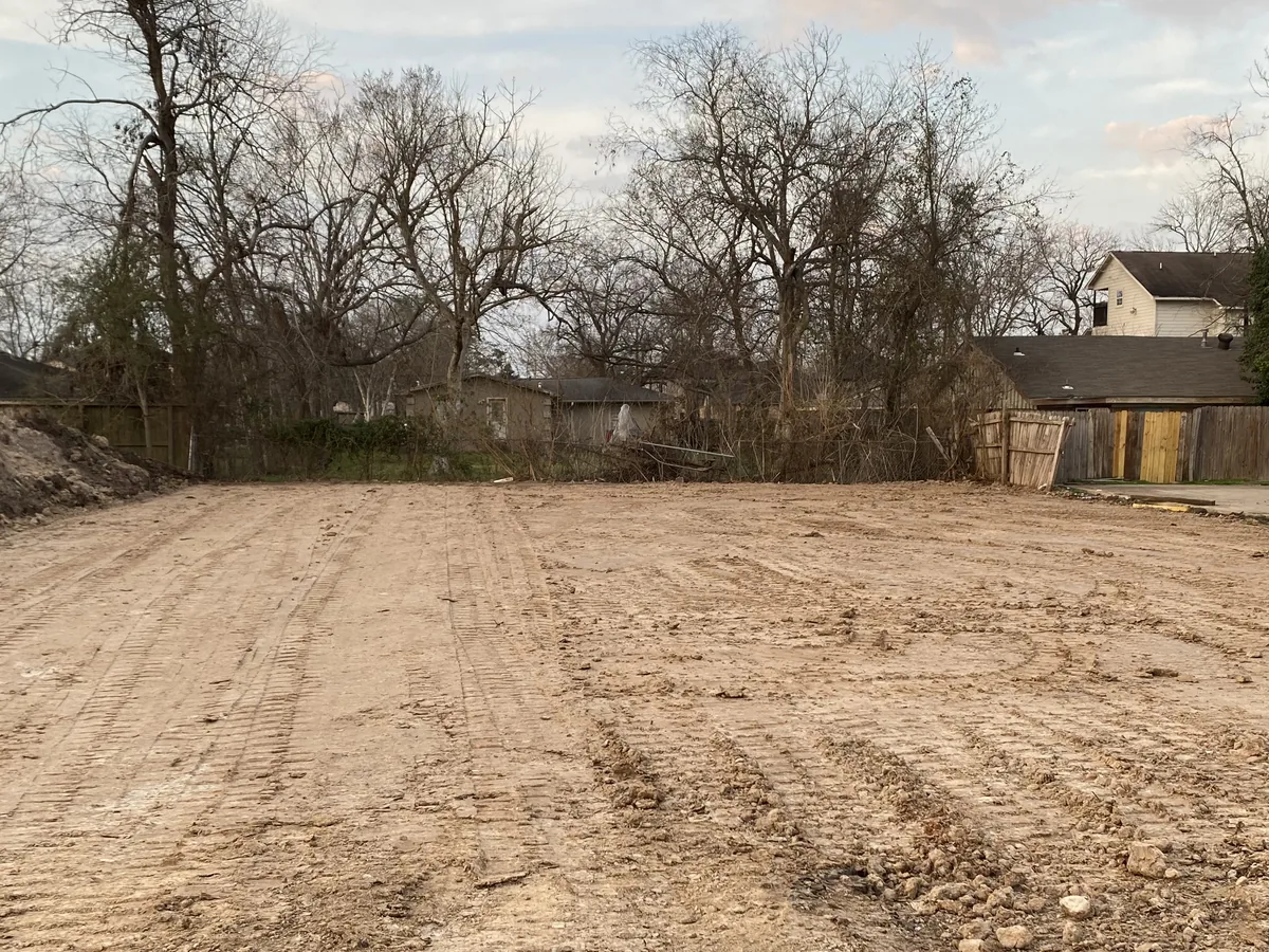 Cleared and graded dirt lot after a teardown with fences and trees around it, demolition