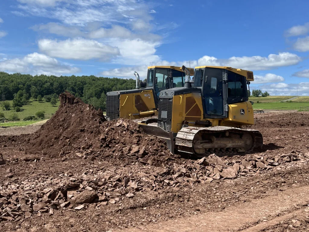 Two crawler dozers pushing broken rock and dirt to build up a pad, oilfield services