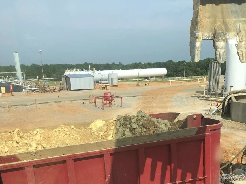 Red dump truck bed loaded with rock at a gas facility with white tanks behind, oilfield services