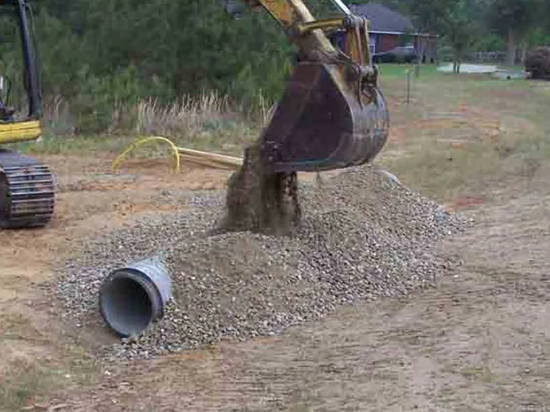Excavator covering a new driveway culvert pipe with gravel at the road entrance, site preparation