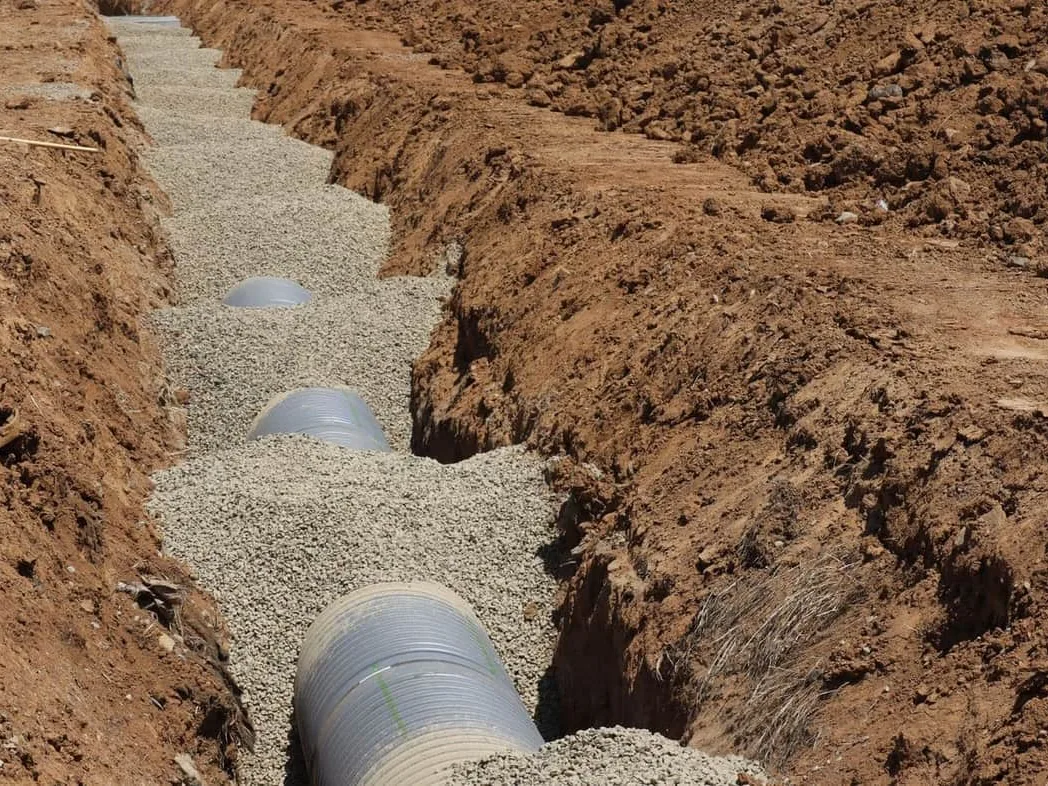 Corrugated pipe bedded in gravel along an open trench cut through clay, underground utilities