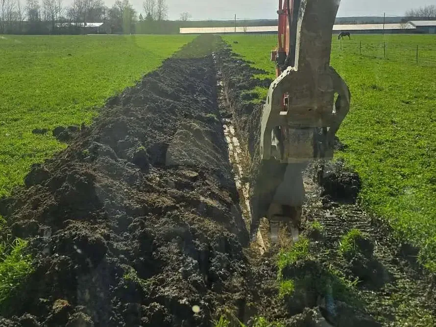 Long trench cut across a pasture with the dirt piled alongside for backfill, underground utilities
